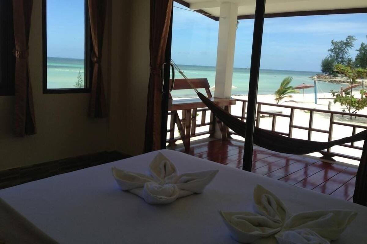A room with a view of the beach, a hammock, and a table with towels.