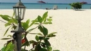 A beach scene with a lamp post and a plant in the foreground, a clear blue sky, and a sandy beach extending to the horizon. - Seaview Rainbow (Ko Pha-ngan)