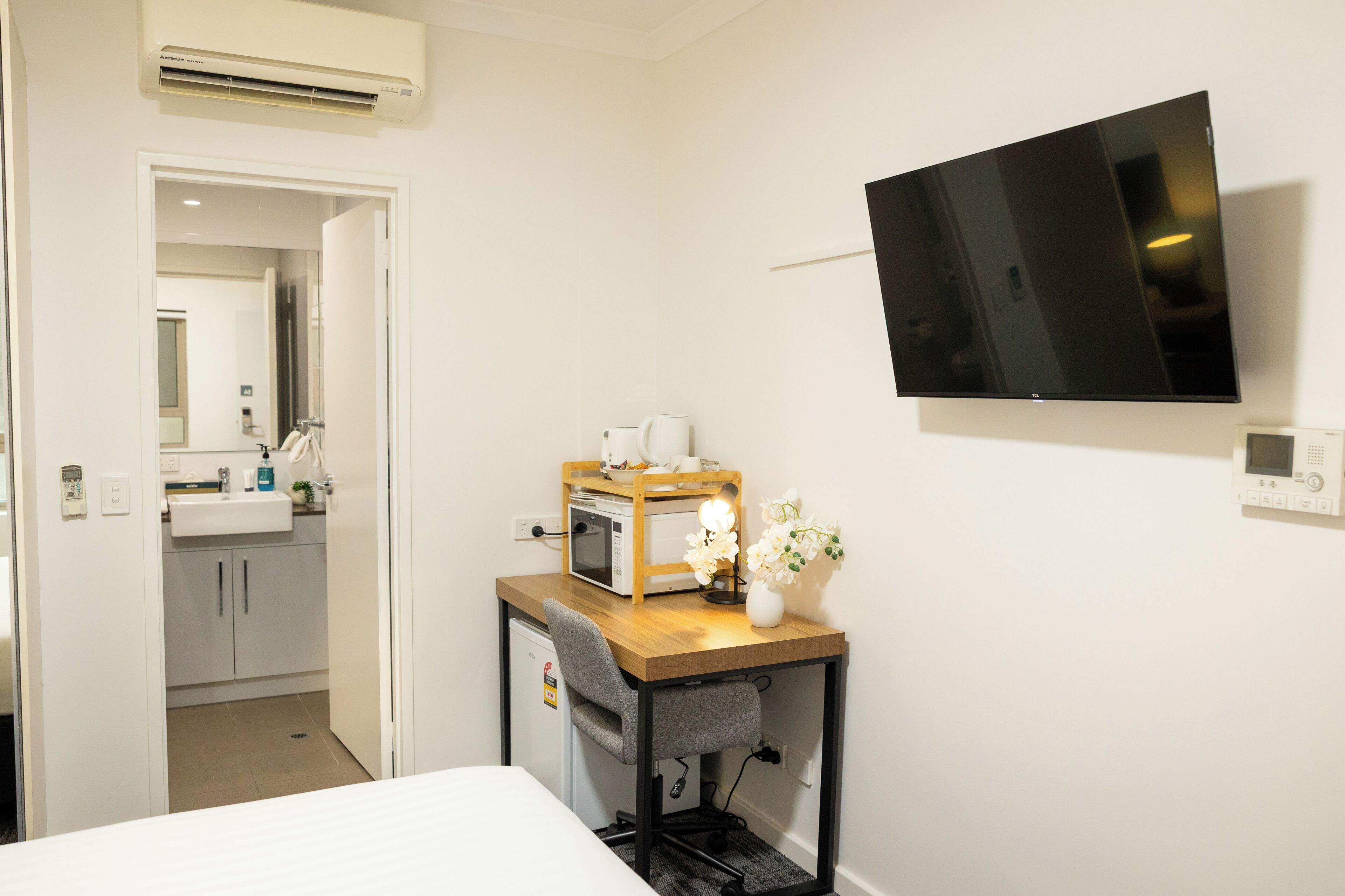 Una habitación de hotel pequeña con cama, escritorio con ordenador, televisión y una kitchenette.