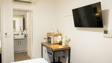 Una habitación de hotel pequeña con cama, escritorio con ordenador, televisión y una kitchenette.
