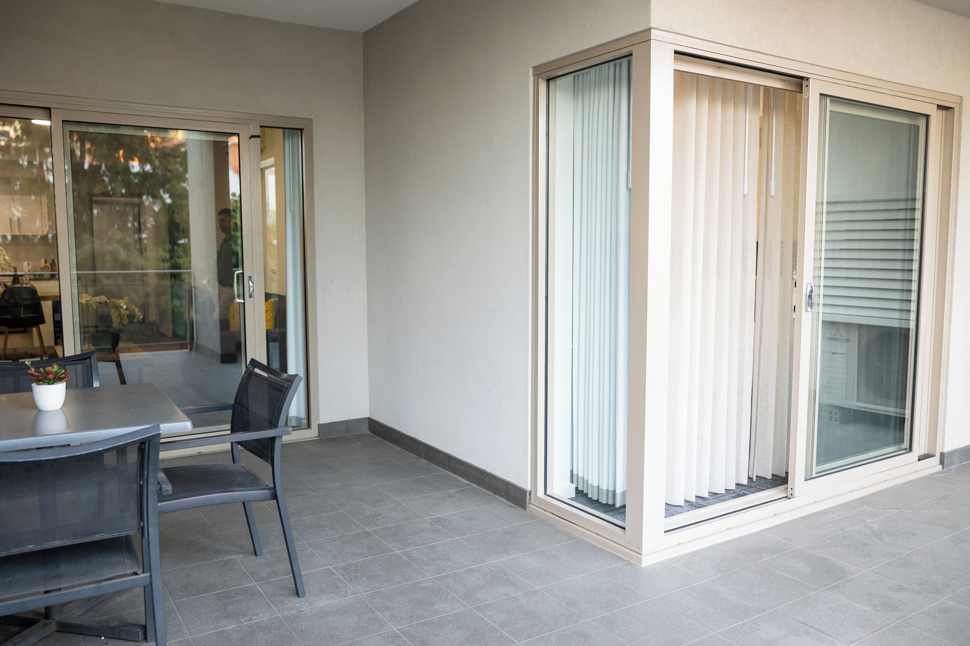 A modern patio area with a table and chairs, a sliding glass door, and a view of the outdoors.