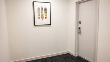 A hallway with a framed artwork of feathers, a door with a numeric keypad, and a carpeted floor.