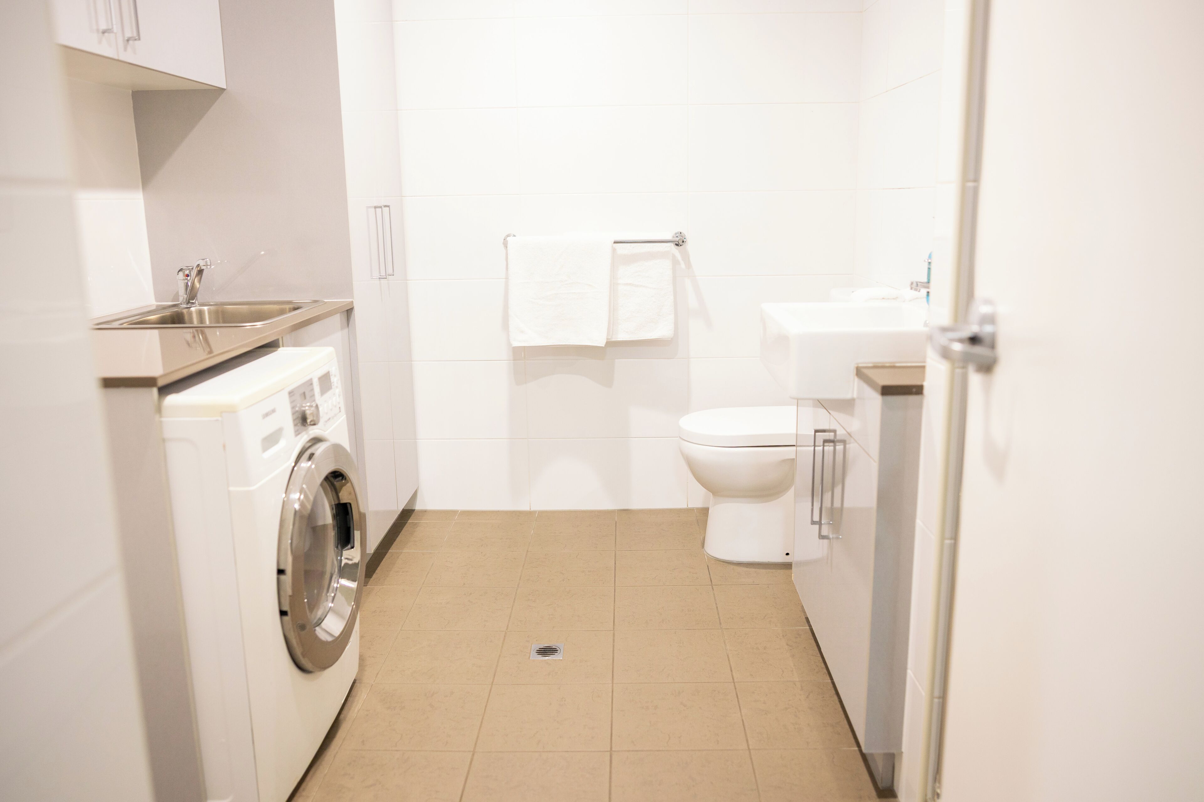 A compact bathroom with a washing machine, toilet, sink, and towel rack.