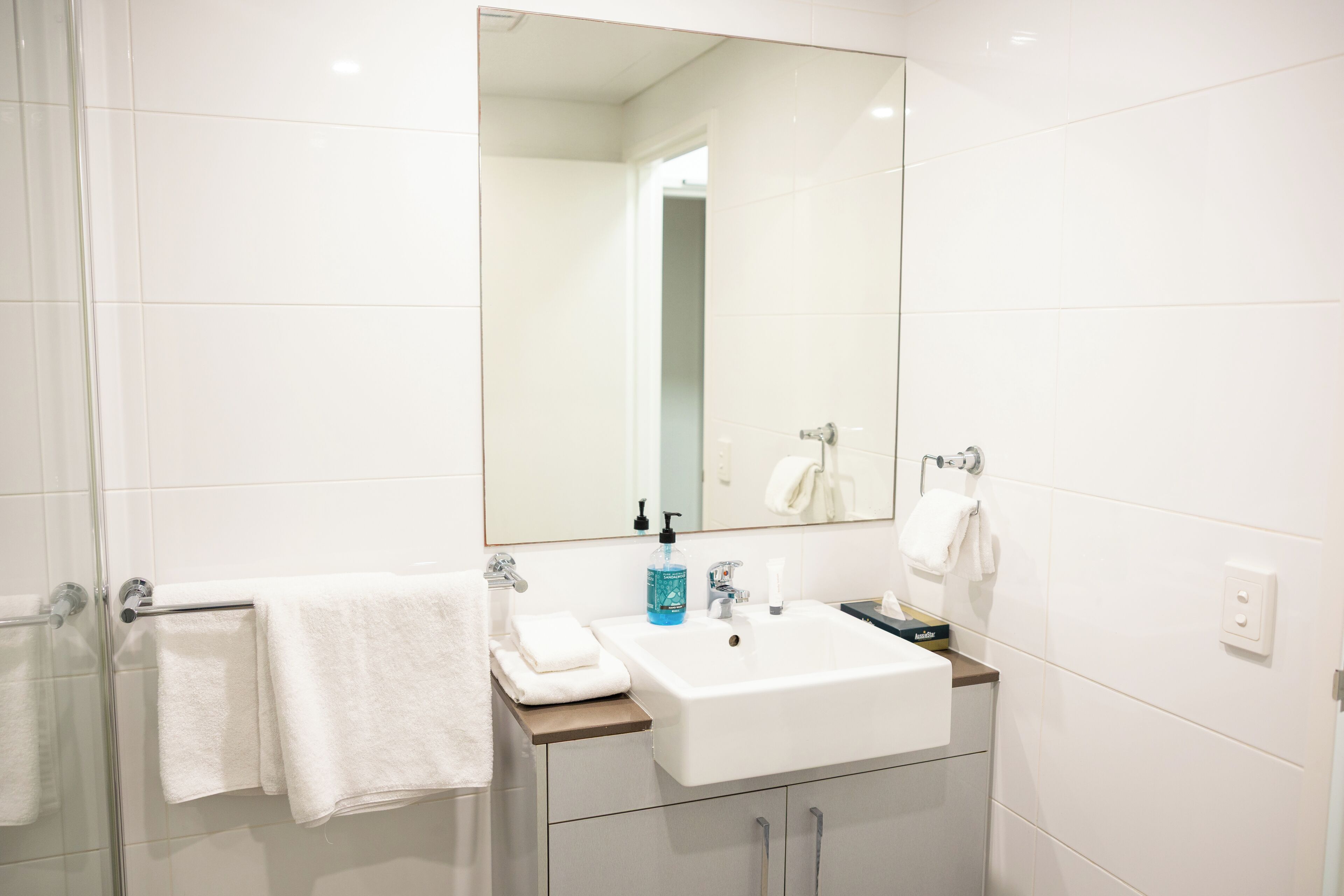 A modern bathroom with a large mirror, white sink, and two towel racks.