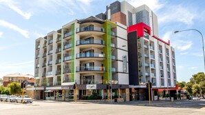A multi-story hotel with balconies, a prominent red and green facade, and a visible sign indicating the name and floor number. - Baileys Serviced Apartments (East Perth)