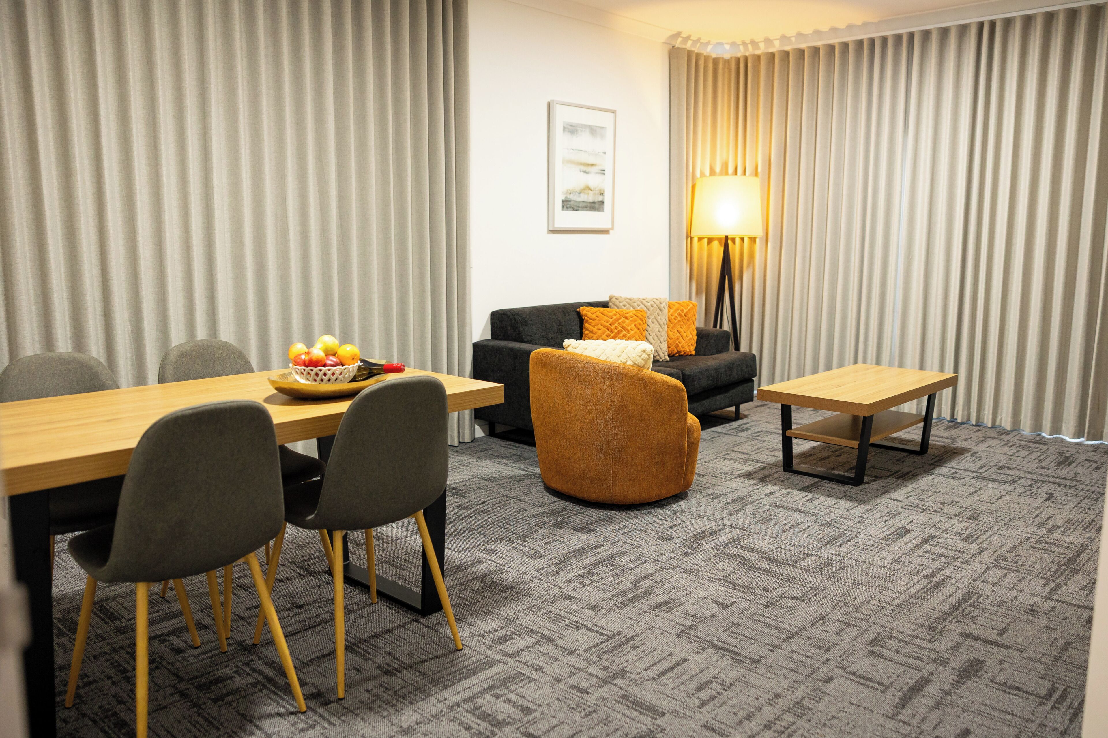 A hotel room with a dining table, chairs, a sofa, a lamp, and a framed picture on the wall.
