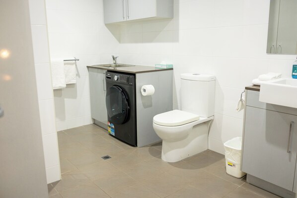 A compact bathroom with a washing machine, toilet, and a small sink.
