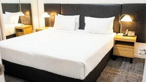 A neatly made bed with white linens, two bedside tables with lamps, and a telephone on one of the tables. - Baileys Serviced Apartments (East Perth)