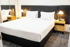A neatly made bed with white linens, two bedside tables with lamps, and a telephone on one of the tables. - Baileys Serviced Apartments (East Perth)