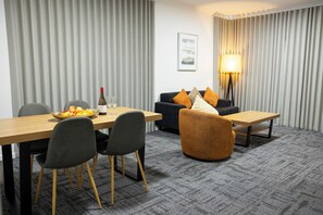 Une chambre d’hôtel équipée d’une table à manger, de chaises, d’un canapé, d’une lampe et d’un tableau encadré au mur.