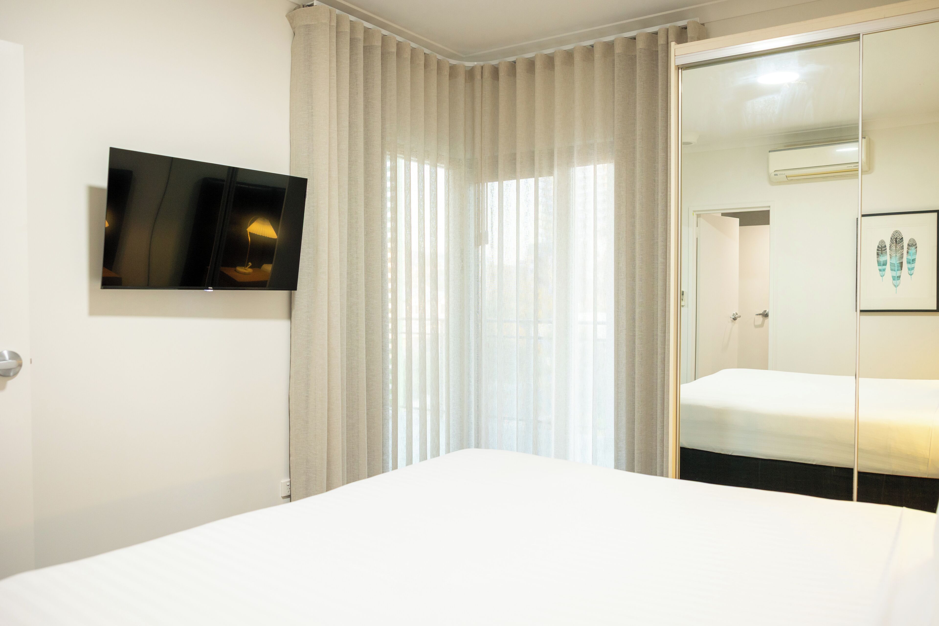 Habitación de hotel con cama, televisor montado en la pared, puerta corrediza de vidrio y un cuadro enmarcado.