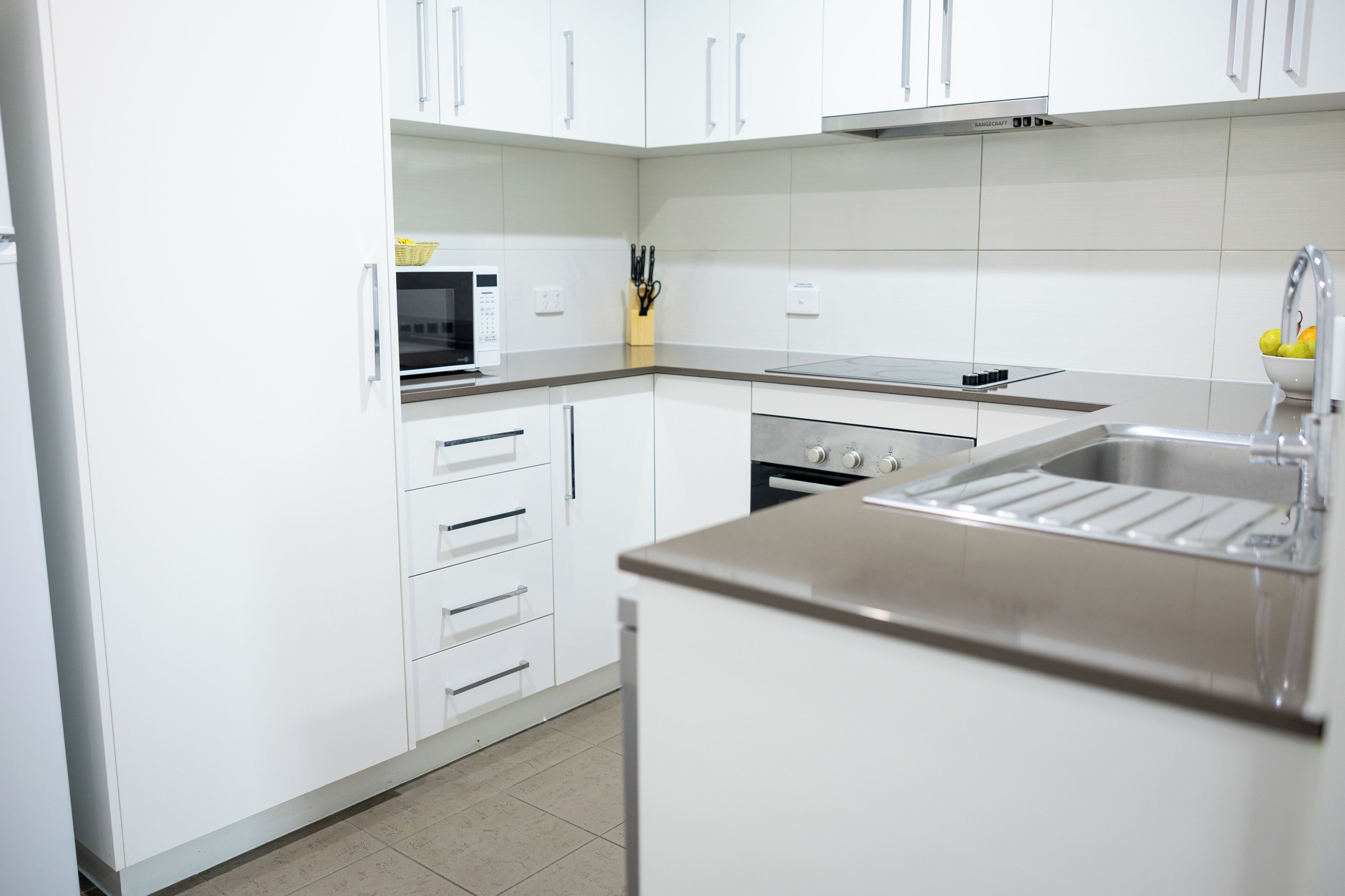 A modern kitchen with white cabinets, a microwave, an oven, and a stainless steel sink.