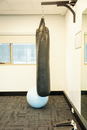 A punching bag hanging from a metal fixture in a room with carpeted flooring, a window, and a mirror on the wall. - Baileys Serviced Apartments (East Perth)