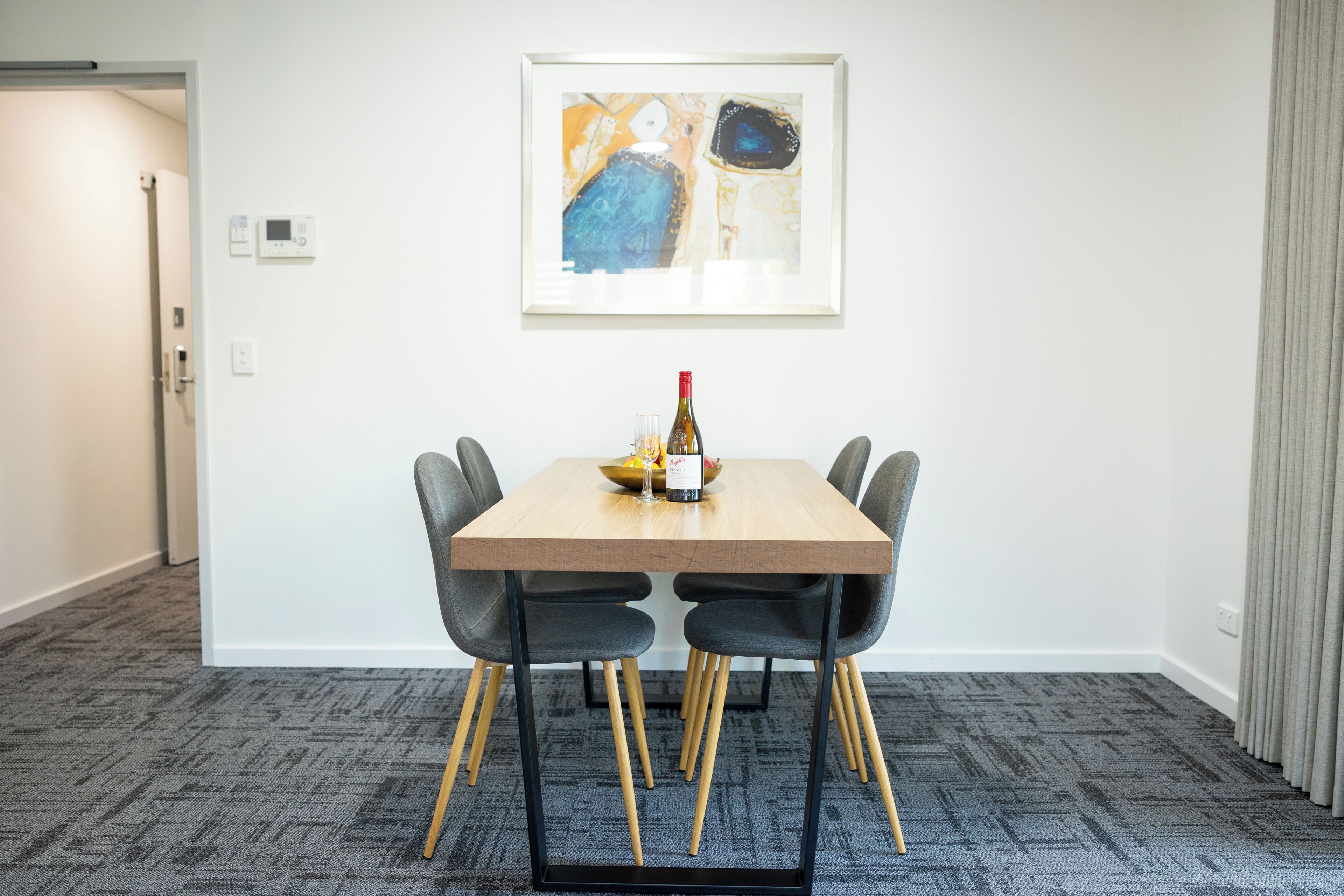 A dining area with a table, chairs, a bottle, and a framed artwork on the wall.