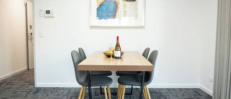 A dining area with a table, chairs, a bottle, and a framed artwork on the wall.