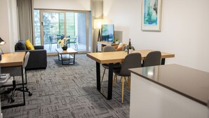 A modern hotel room with a dining area, a sofa, a table, and a large window with blinds. - Baileys Serviced Apartments (East Perth)