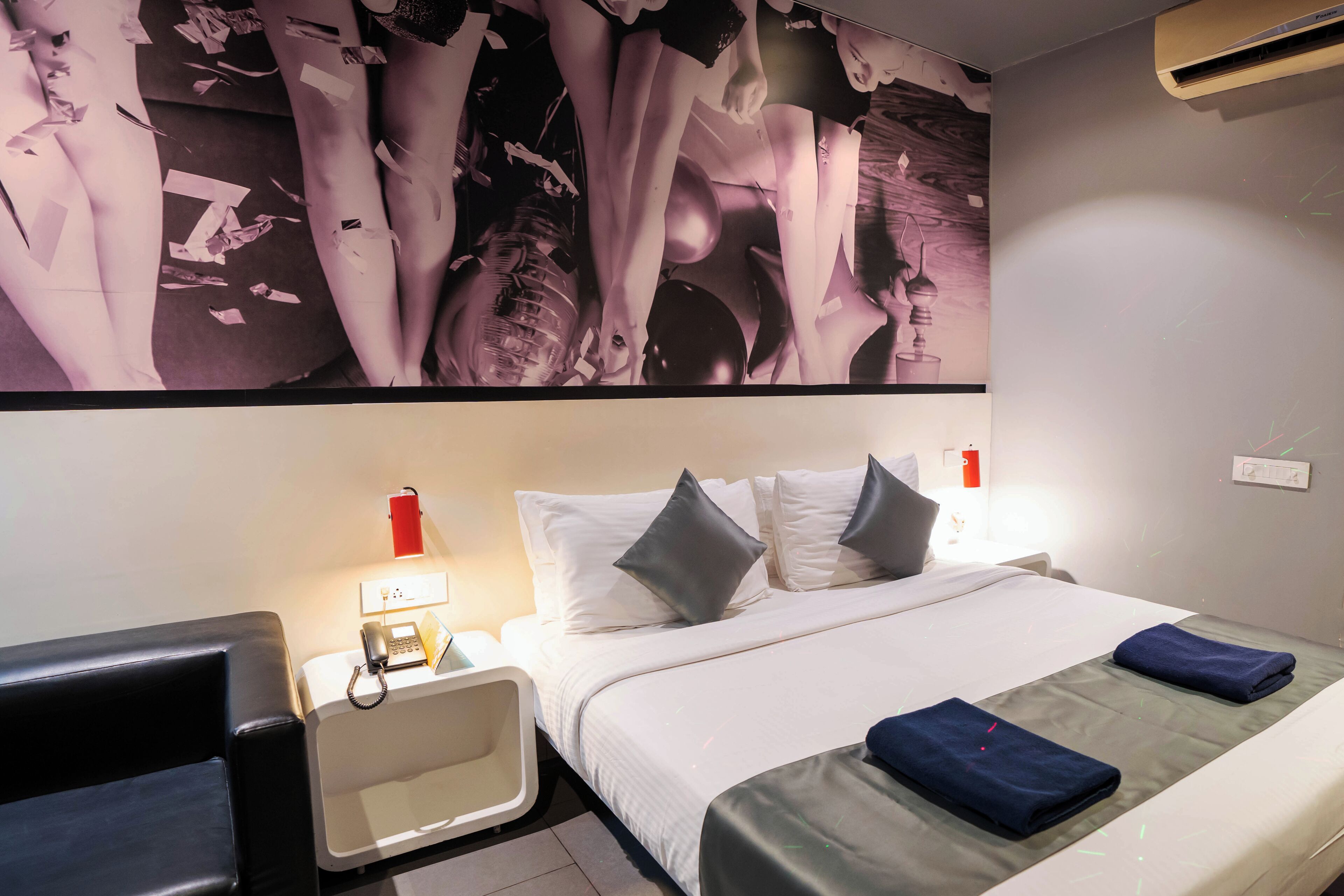 Habitación de hotel con una cama grande, una mesita de noche con lámpara, un teléfono y un aire acondicionado de pared.