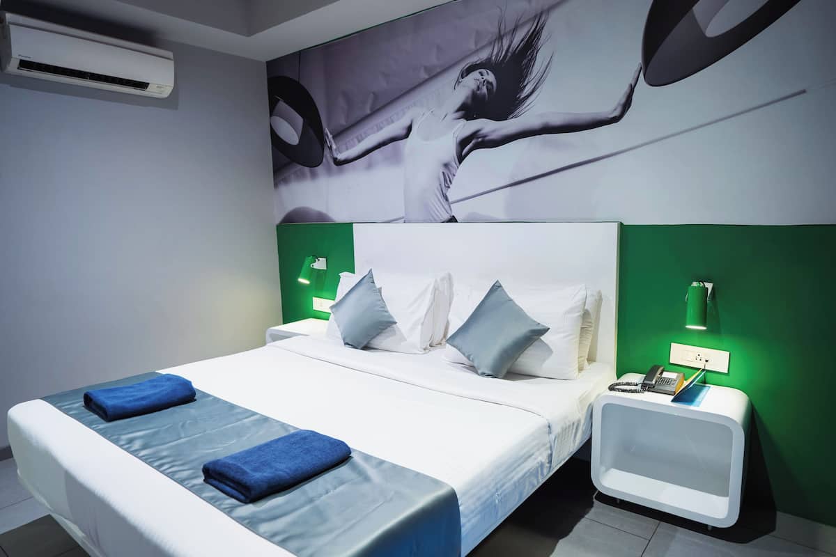 A modern hotel room with a large bed, two pillows, a nightstand with a lamp, and a green accent wall.