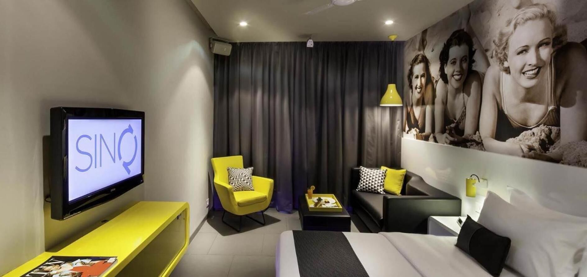 Ein modernes Hotelzimmer mit einem Bett, einer Couch, einem gelben Sessel, einem Fernseher und einem großen Wandbild.