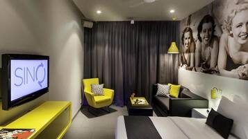 Ein modernes Hotelzimmer mit einem Bett, einer Couch, einem gelben Sessel, einem Fernseher und einem großen Wandbild.