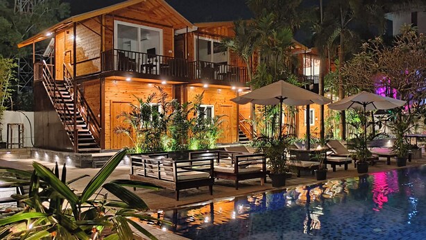 A wooden villa with a pool, outdoor seating, and a staircase leading to a balcony. - SinQ Party Hotel (Candolim)
