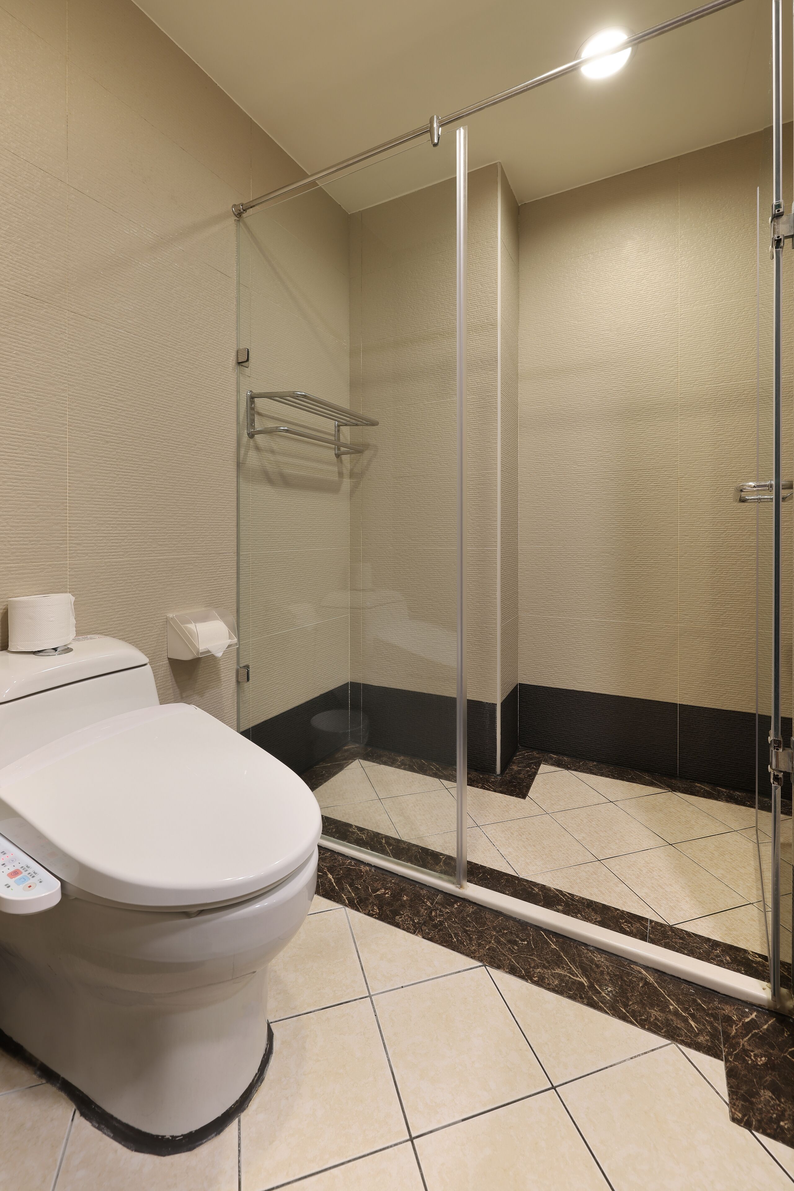 Une salle de bain moderne dotée d’une douche à parois de verre, de toilettes avec panneau de commande et d’un porte-serviettes.