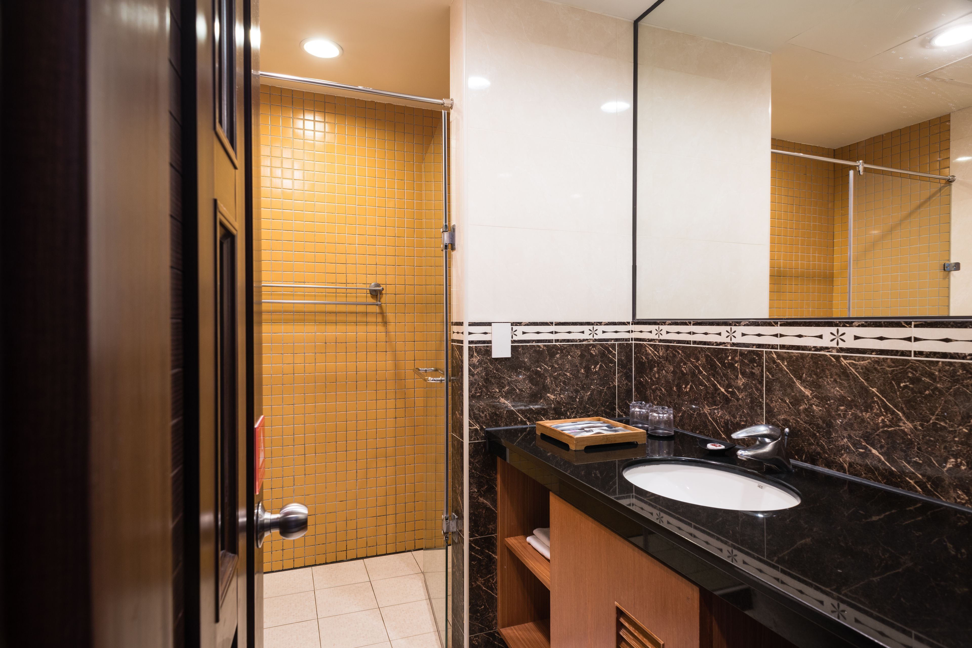 Un baño moderno con lavamanos de encimera negro, espejo y paredes de azulejos amarillos.