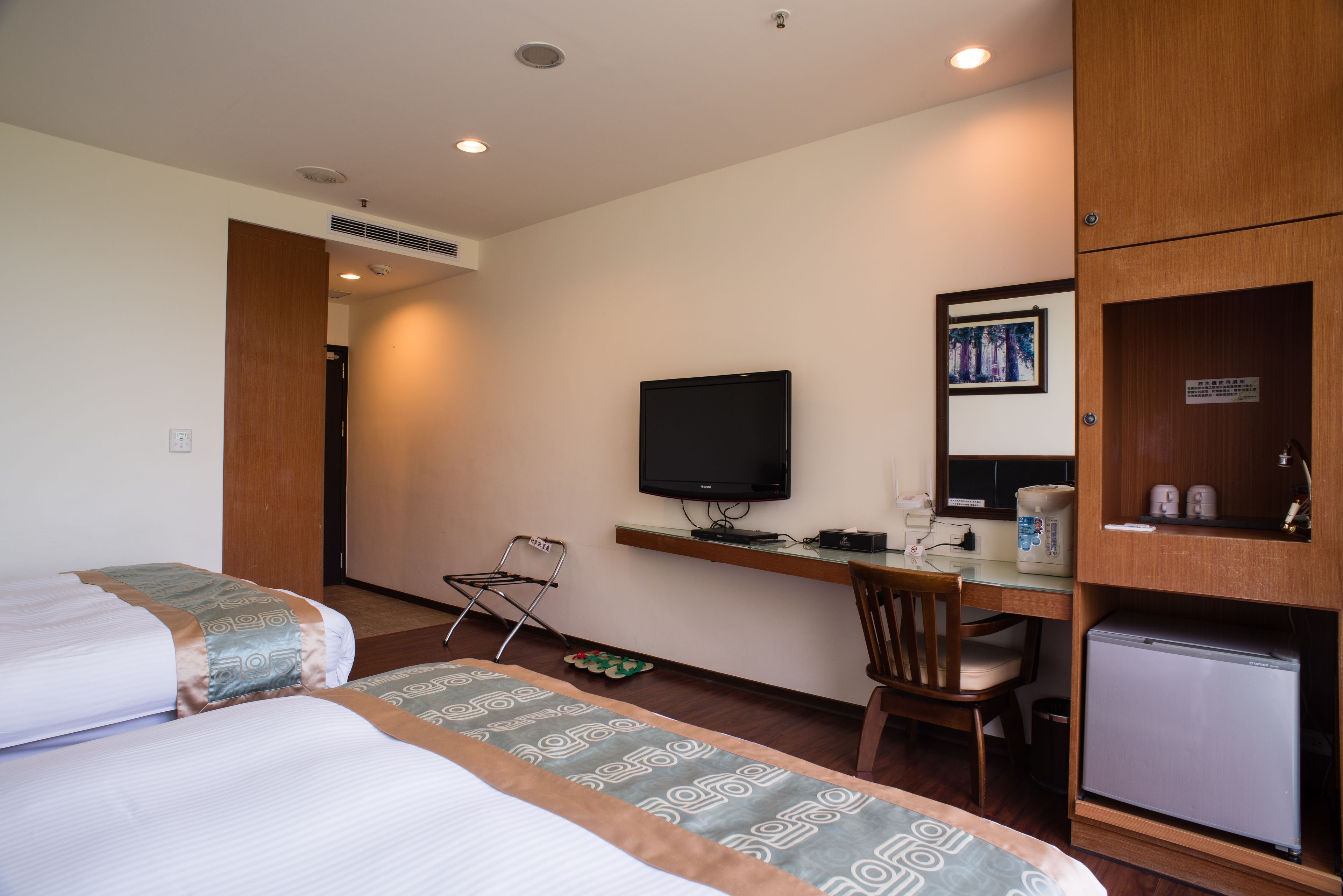 A hotel room with two beds, a desk with a computer, a television, and a refrigerator.