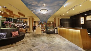 Um hall de hotel com uma recepção central, área de estar com sofá e almofadas, exposição de bolsas e teto com design de nuvens.