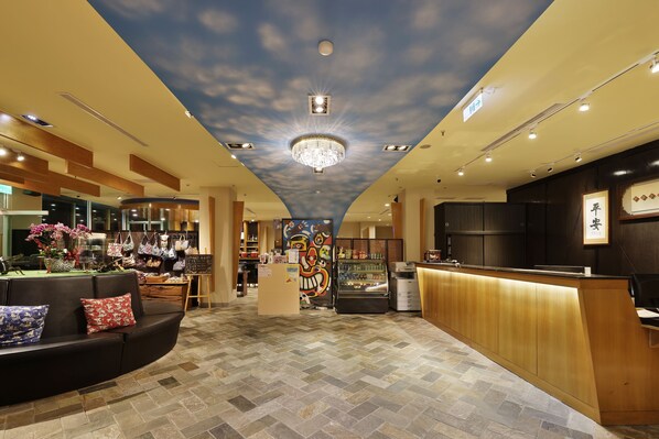 A hotel lobby with a central reception desk, a seating area with a sofa and cushions, a display of handbags, and a ceiling with a cloud design. - Shante Hotel Chitou Nantou (Lugu)