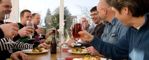 A group of people toasting with wine glasses at a table with plates of food and a bottle of beer.