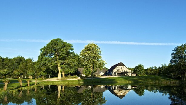 A large house with a stone facade, surrounded by a pond and trees, with a clear sky above. - Nötesjö Hotell (Svedala)
