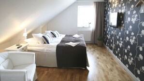 A bedroom with a bed, a bedside table with a lamp, a TV mounted on the wall, and a window with curtains. - Nötesjö Hotell (Svedala)