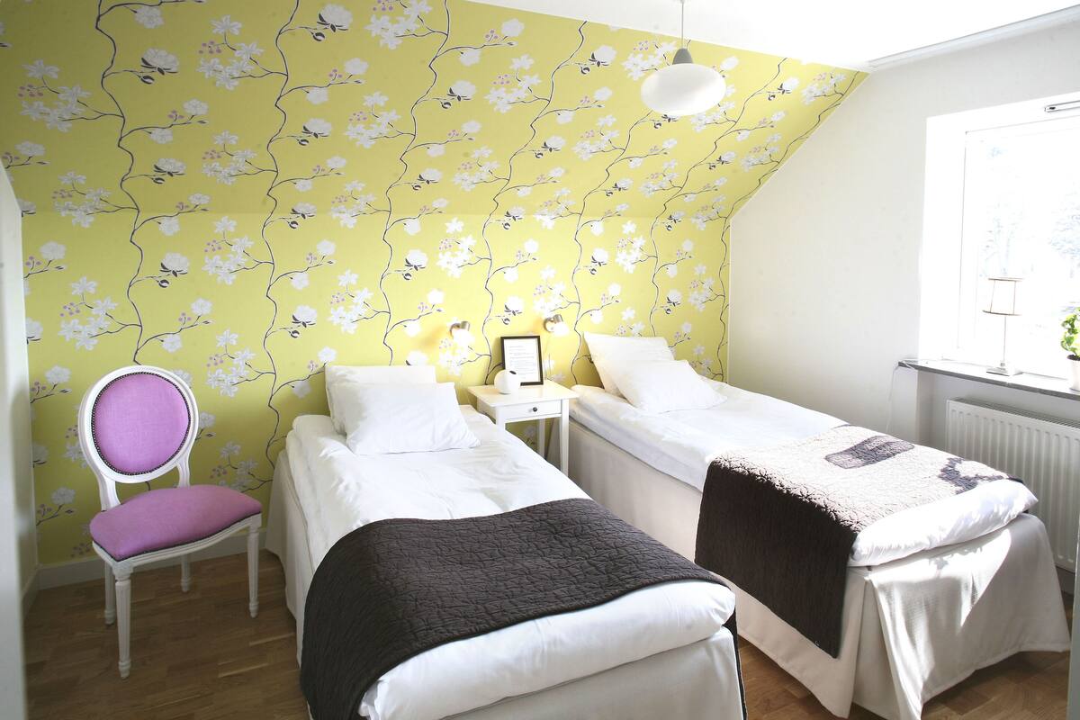 A bedroom with two beds, a chair, a nightstand, and a radiator.
