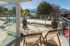 Un balcón con puerta de vidrio, plantas en macetas, piscina y vistas a montañas.