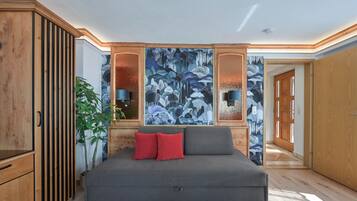 A modern bedroom with a grey sofa bed, a large abstract painting, wooden paneling, and a potted plant.