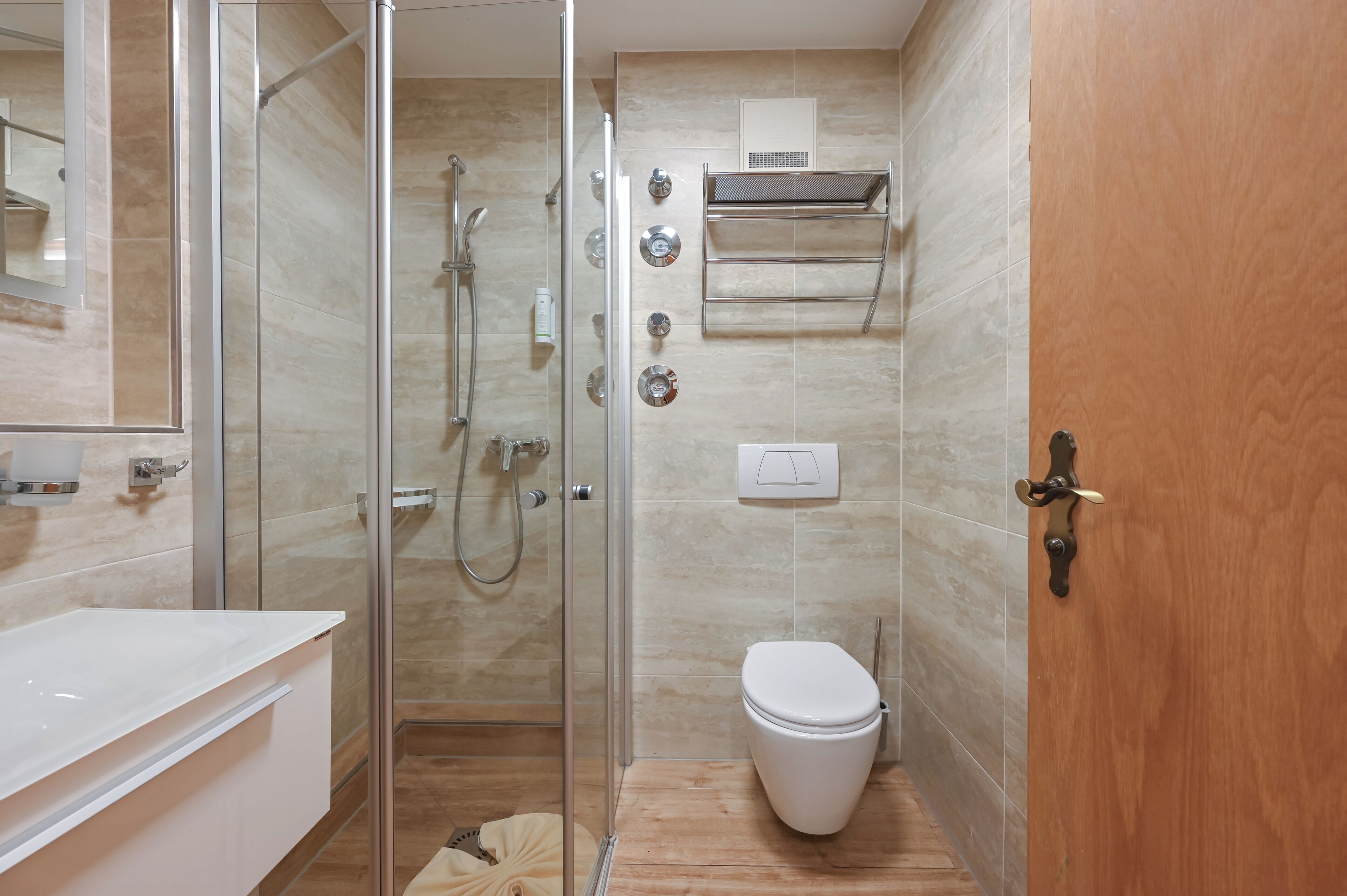 Un baño moderno con ducha envuelta en vidrio, inodoro blanco y puerta de madera.