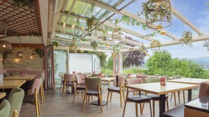A restaurant with outdoor seating, wooden tables and chairs, hanging plants, and a view of the outdoors. - Hotel San Marco (Fuessen)