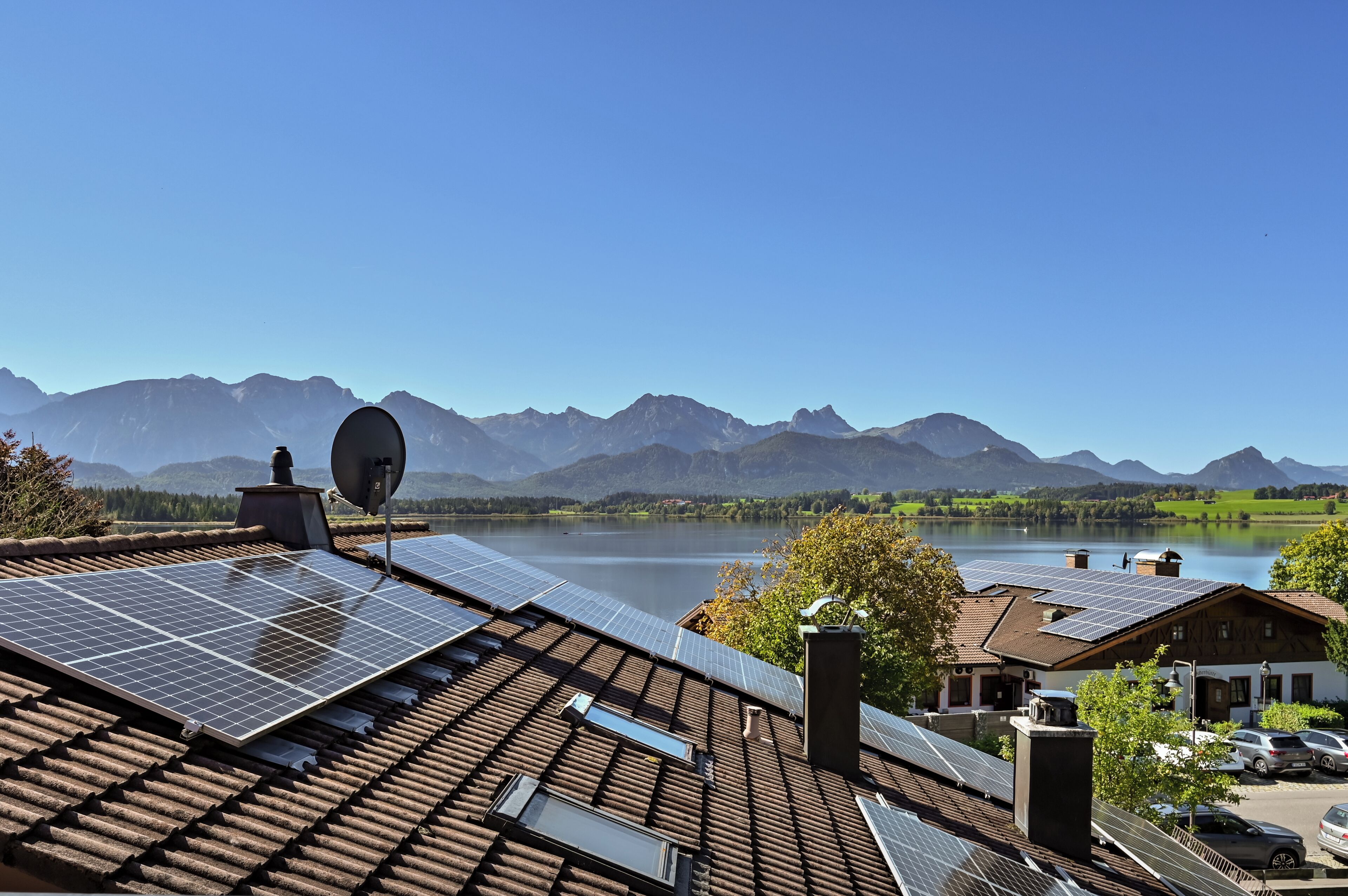 Een gebouw met zonnepanelen op het dak, een schotelantenne en uitzicht op bergen en een meer.