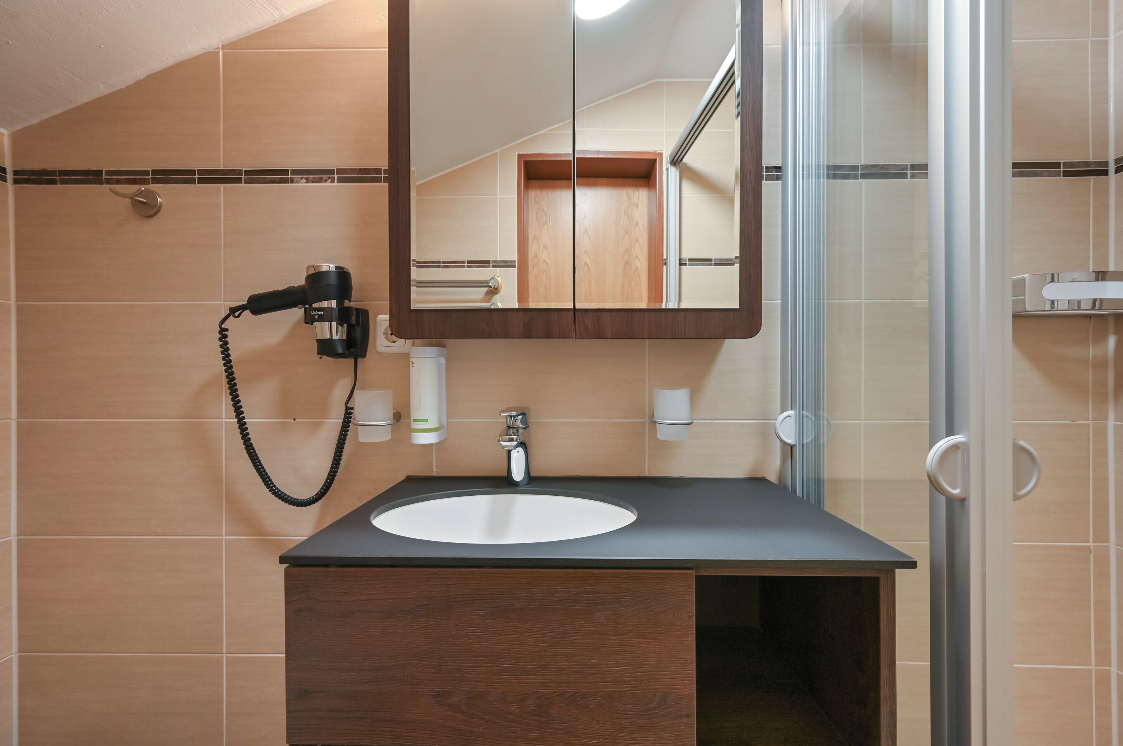 Un bagno con un mobile contenitore in legno, un lavandino, uno specchio e un asciugacapelli a parete.