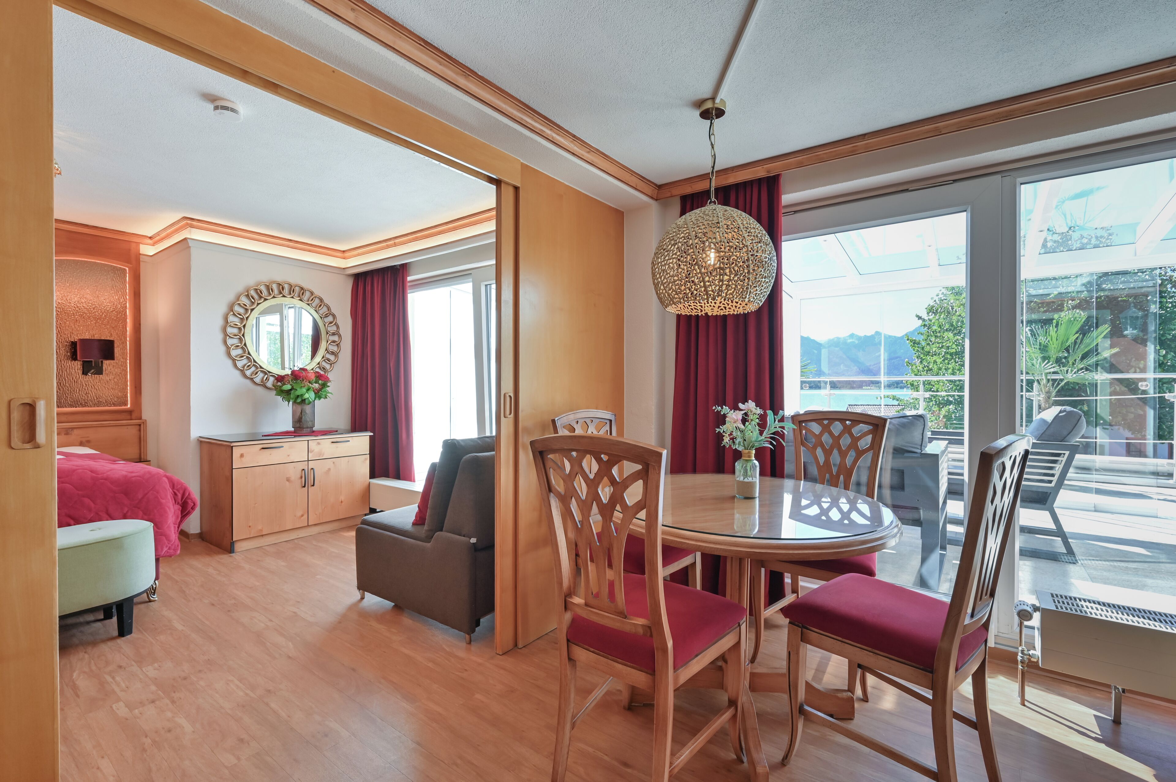 Een hotelkamer met houten vloer, een eettafel met stoelen, een bank, een bed, een spiegel en uitzicht op het omliggende landschap.