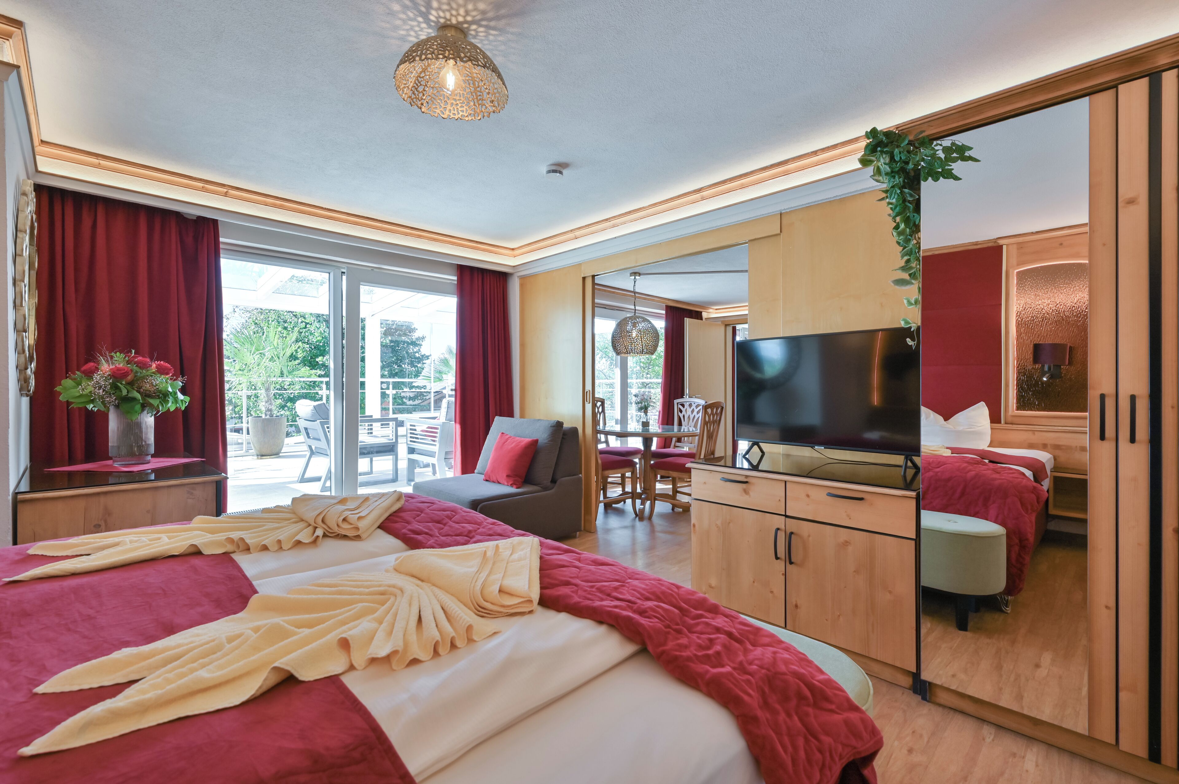 Ein modernes Hotelzimmer mit einem großen Bett, einem Fernseher, einem Essbereich und einem Balkon mit roten Vorhängen.