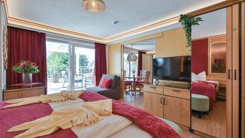 Ein modernes Hotelzimmer mit einem großen Bett, einem Fernseher, einem Essbereich und einem Balkon mit roten Vorhängen.