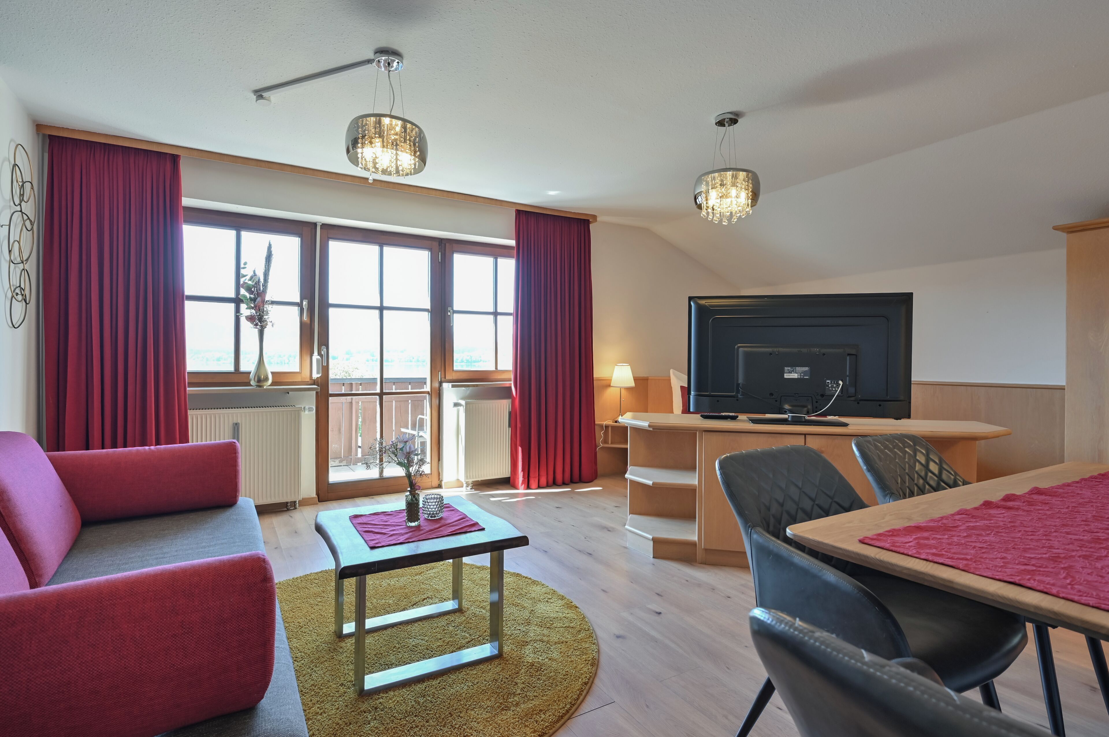 Een moderne woonkamer met een bank, een tafel en een televisie. Er is een balkon met uitzicht.