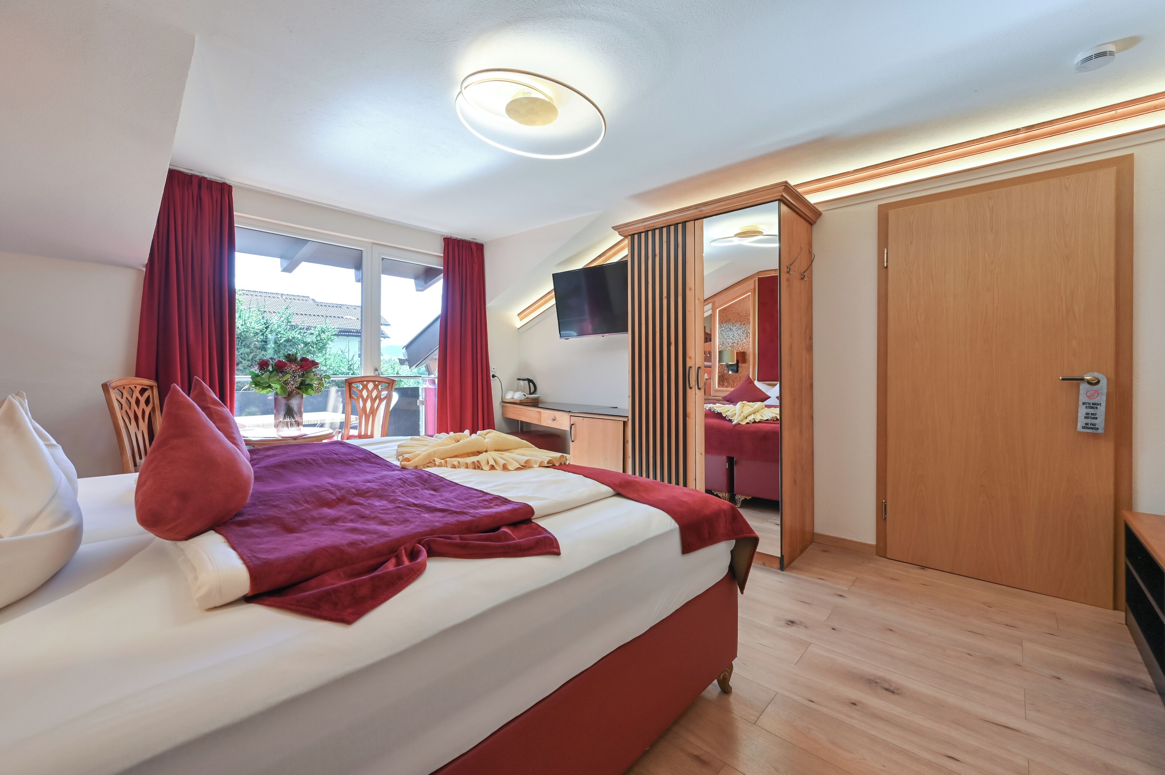 Ein Hotelzimmer mit einem Bett, einem Schreibtisch, einem Fernseher und einer Schiebetür zu einem anderen Raum.