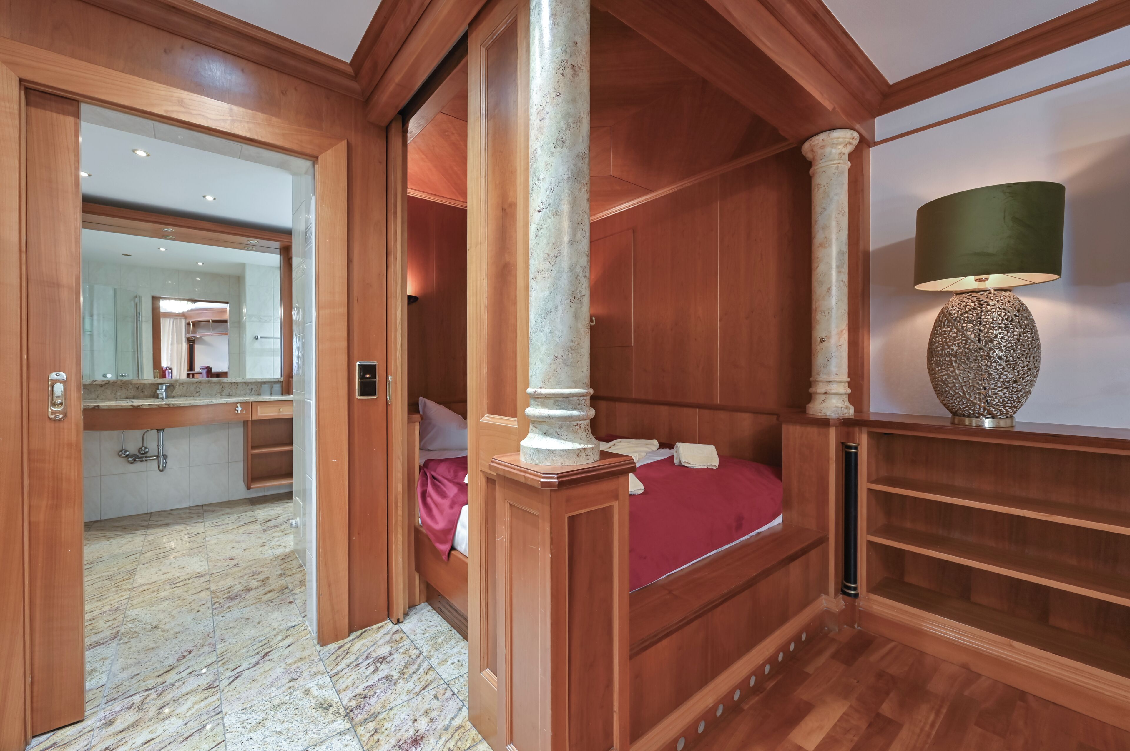 A bedroom with a wooden bed, a nightstand, a lamp, and a large mirror.