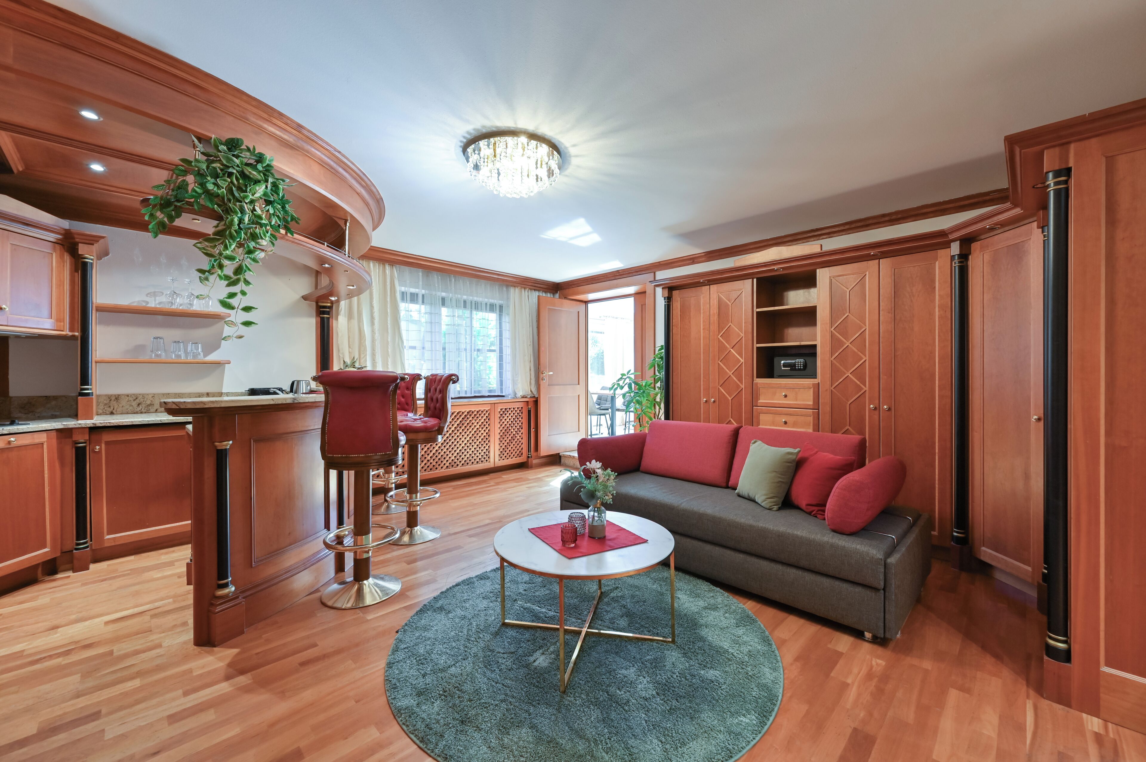 A spacious living area with a wooden floor, a round coffee table, a sofa with red cushions, and a chandelier.