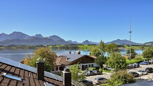 A hotel with solar panels on the roof, a parking area, and a view of a lake and mountains. - Hotel San Marco (Fuessen)