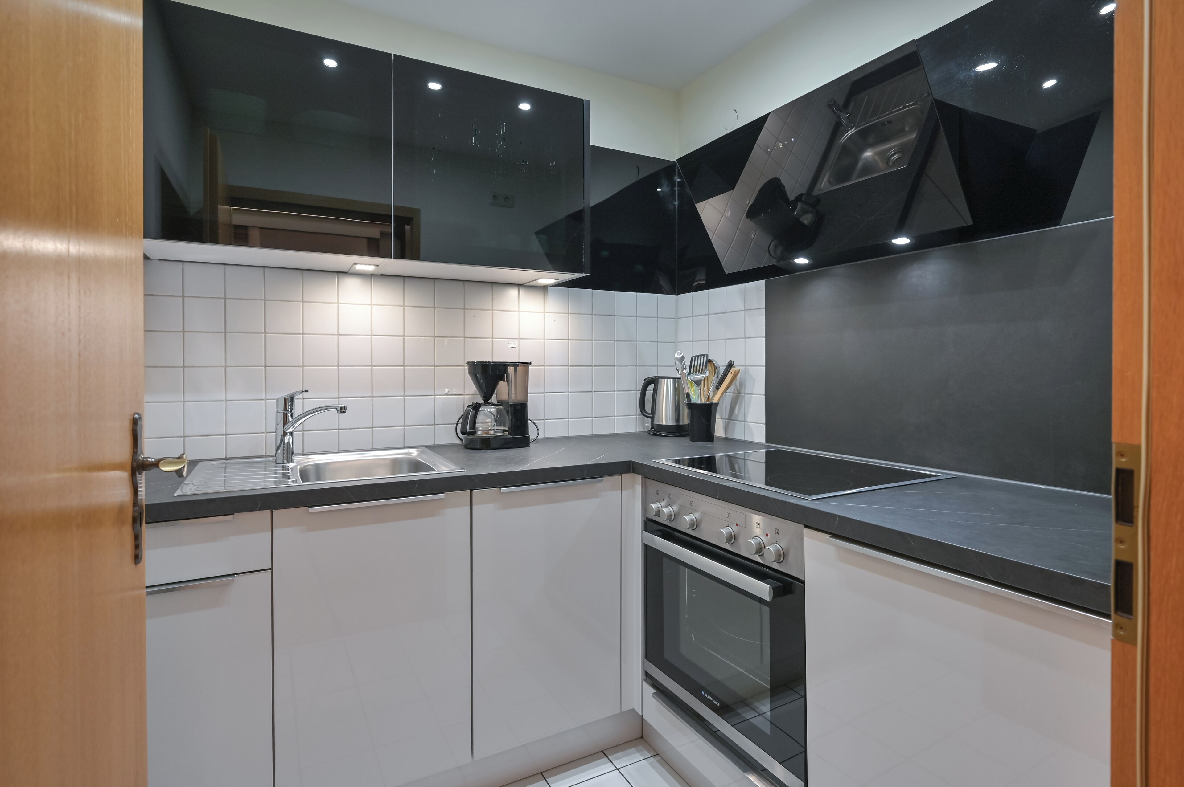 A modern kitchen with white cabinets, a black countertop, a stainless steel sink, and a built-in oven.