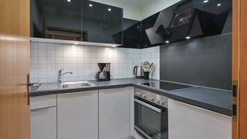 A modern kitchen with white cabinets, a black countertop, a stainless steel sink, and a built-in oven.